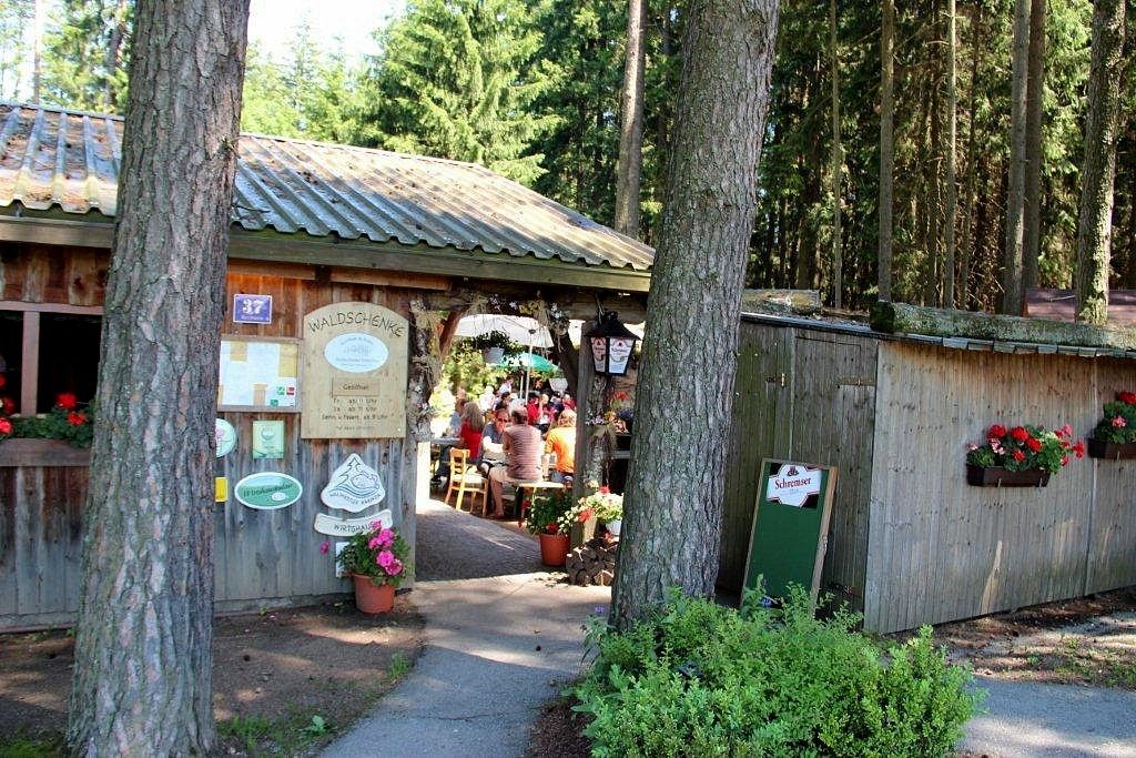 Eingang zu einer Waldschenke mit Holzhütte und Blumen.