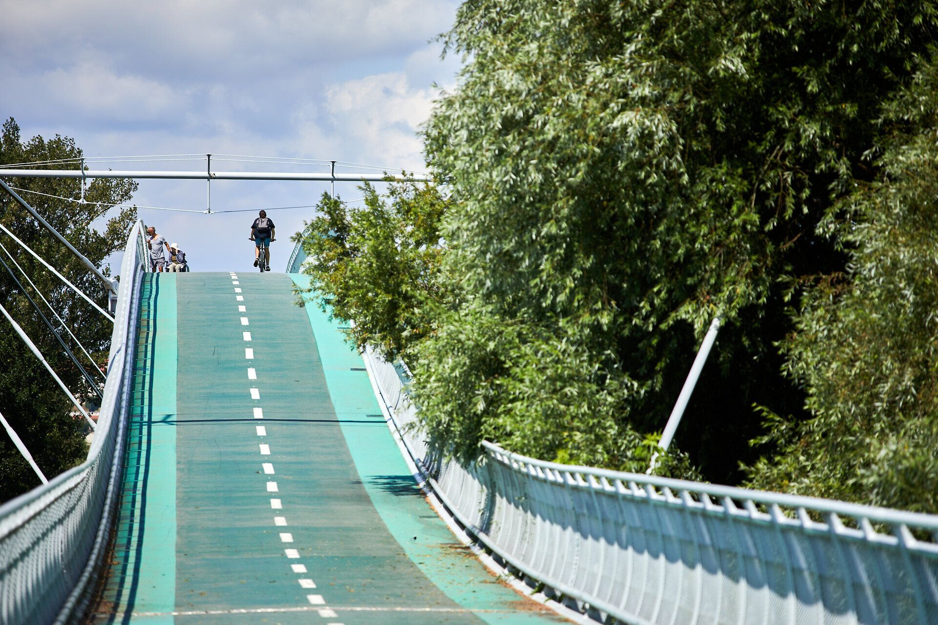 Die sanfte Erhebung der Radwegbrücke lädt Radfahrer ein, die malerische Landschaft zu erkunden. Umgeben von üppigem Grün und dem sanften Rauschen der Bäume, bietet dieser Ort eine perfekte Kulisse für unvergessliche Ausflüge in die Natur.