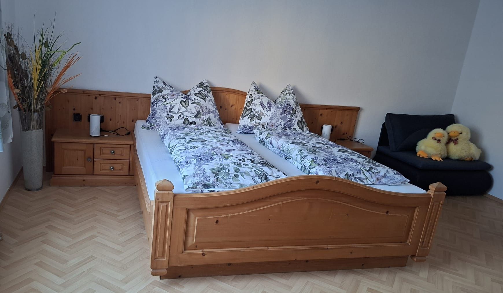 Schlafzimmer mit Doppelbett, Holzmöbeln und zwei Plüschenten auf einem Sofa.