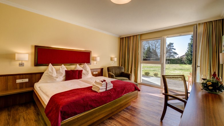 Cozy hotel room with double bed, red accents and a view of the garden through large windows.
