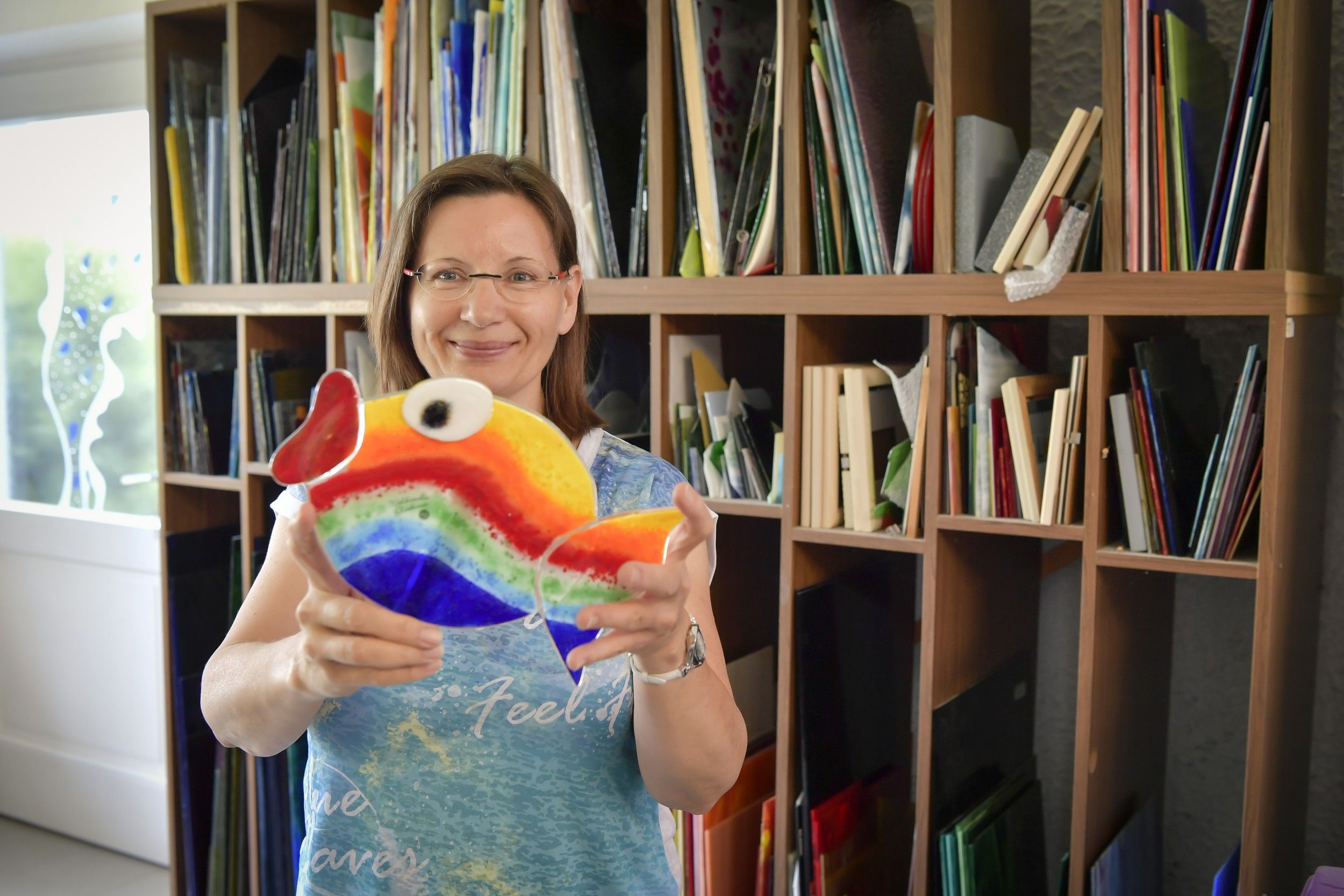 Frau hält bunten Glasfisch in einem Atelier.