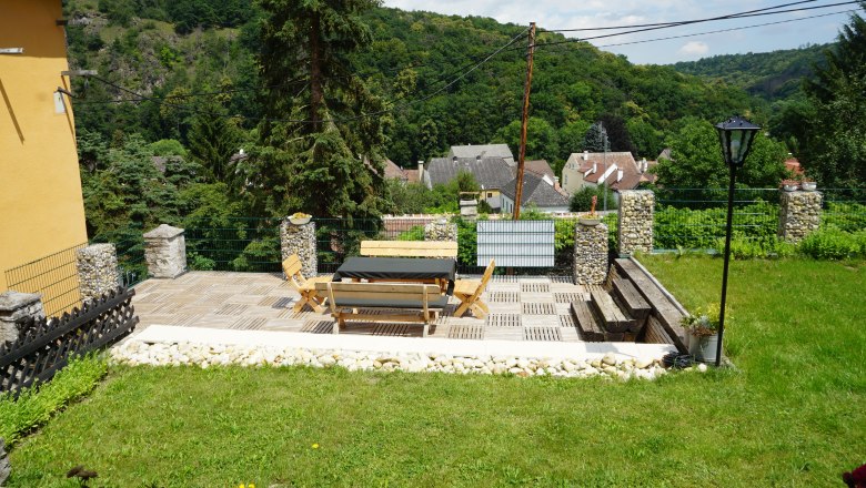 Terrace with wooden furniture and views of a village and wooded hills.
