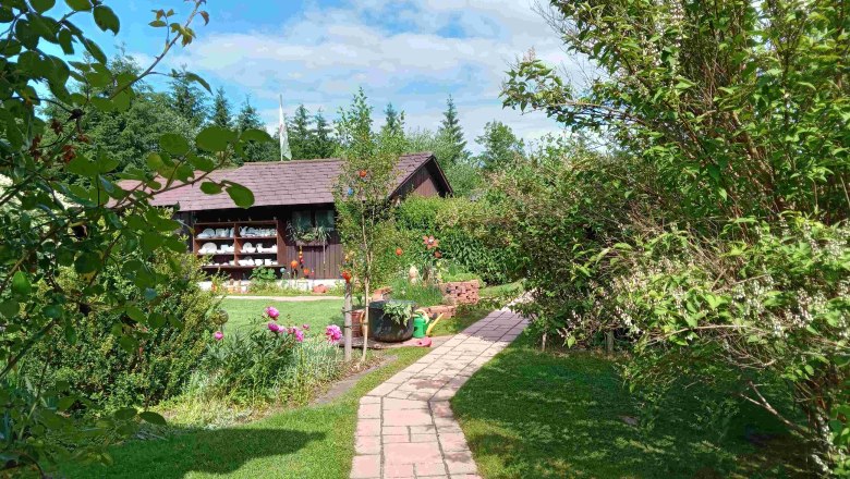 Garten mit Weg, Blumen und Holzhütte im Hintergrund.