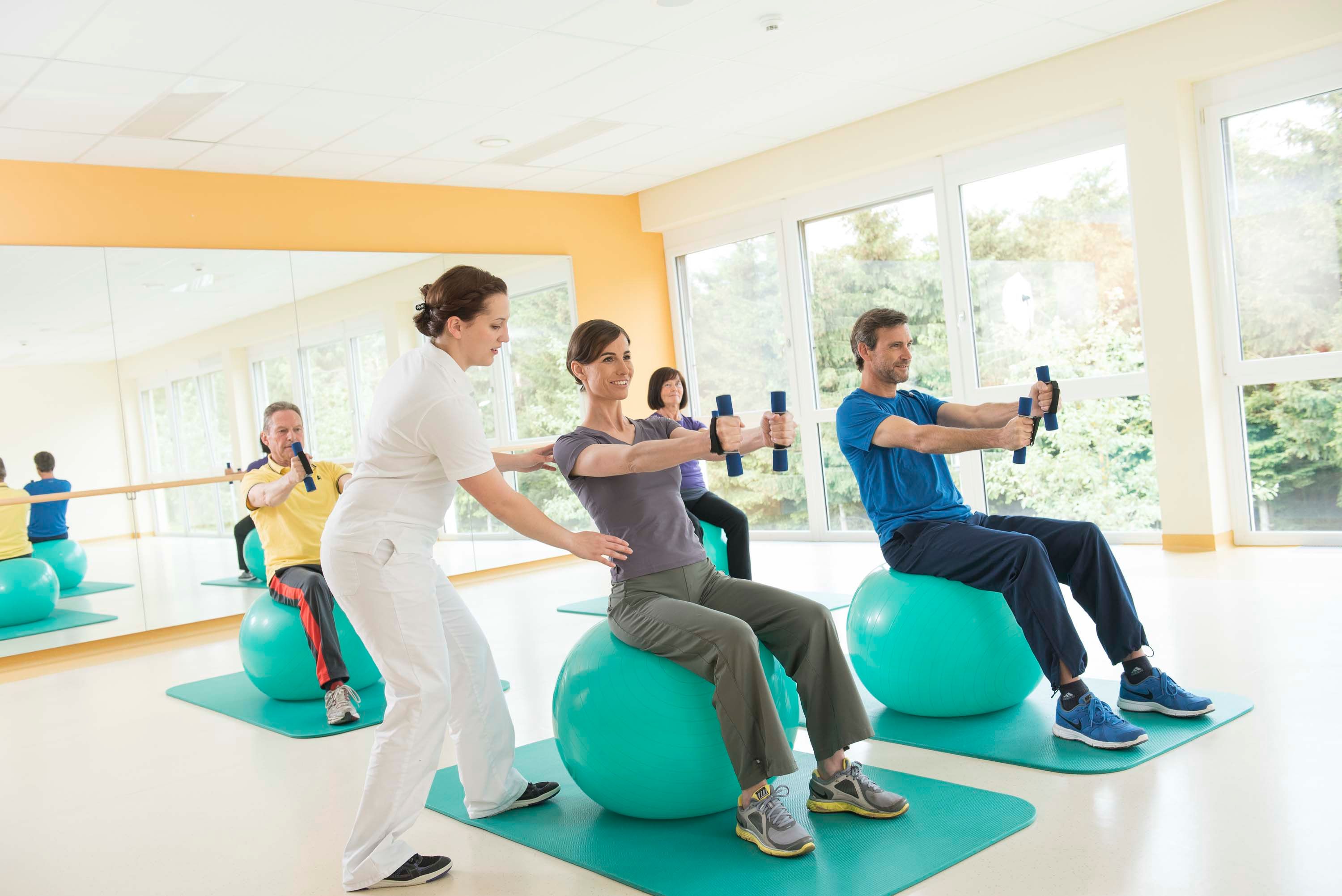 Menschen bei der Heilgymnastik auf Gymnastikbällen mit Hanteln.