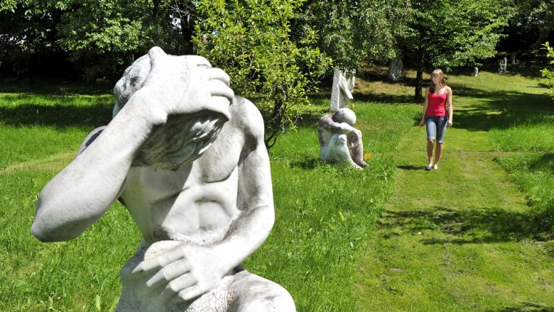 Eine Frau spaziert durch einen Garten mit mehreren Skulpturen auf einer grünen Wiese.