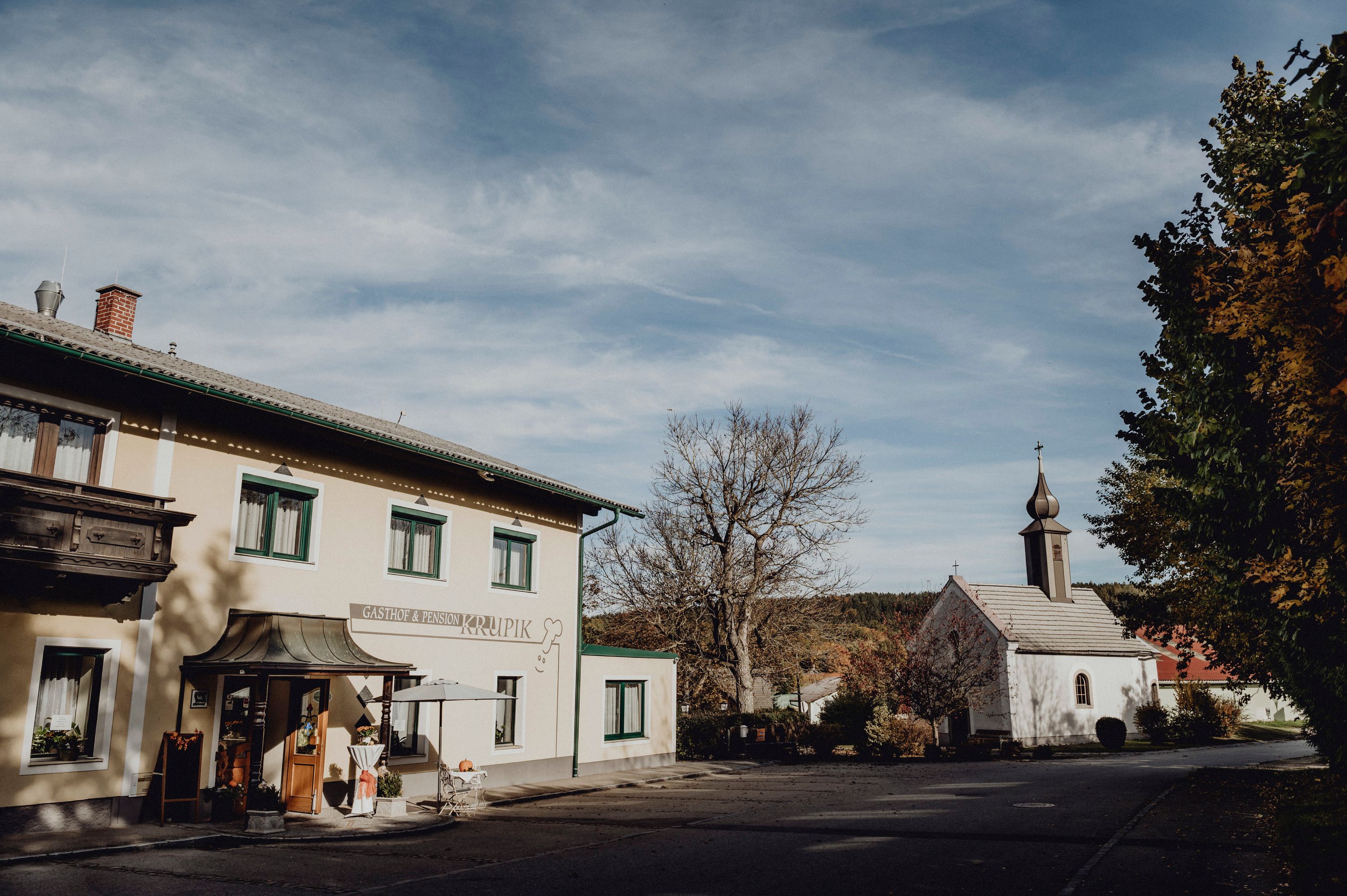 Gasthof und Kirche in Steinbach bei Nagelberg, umgeben von Bäumen und blauem Himmel.