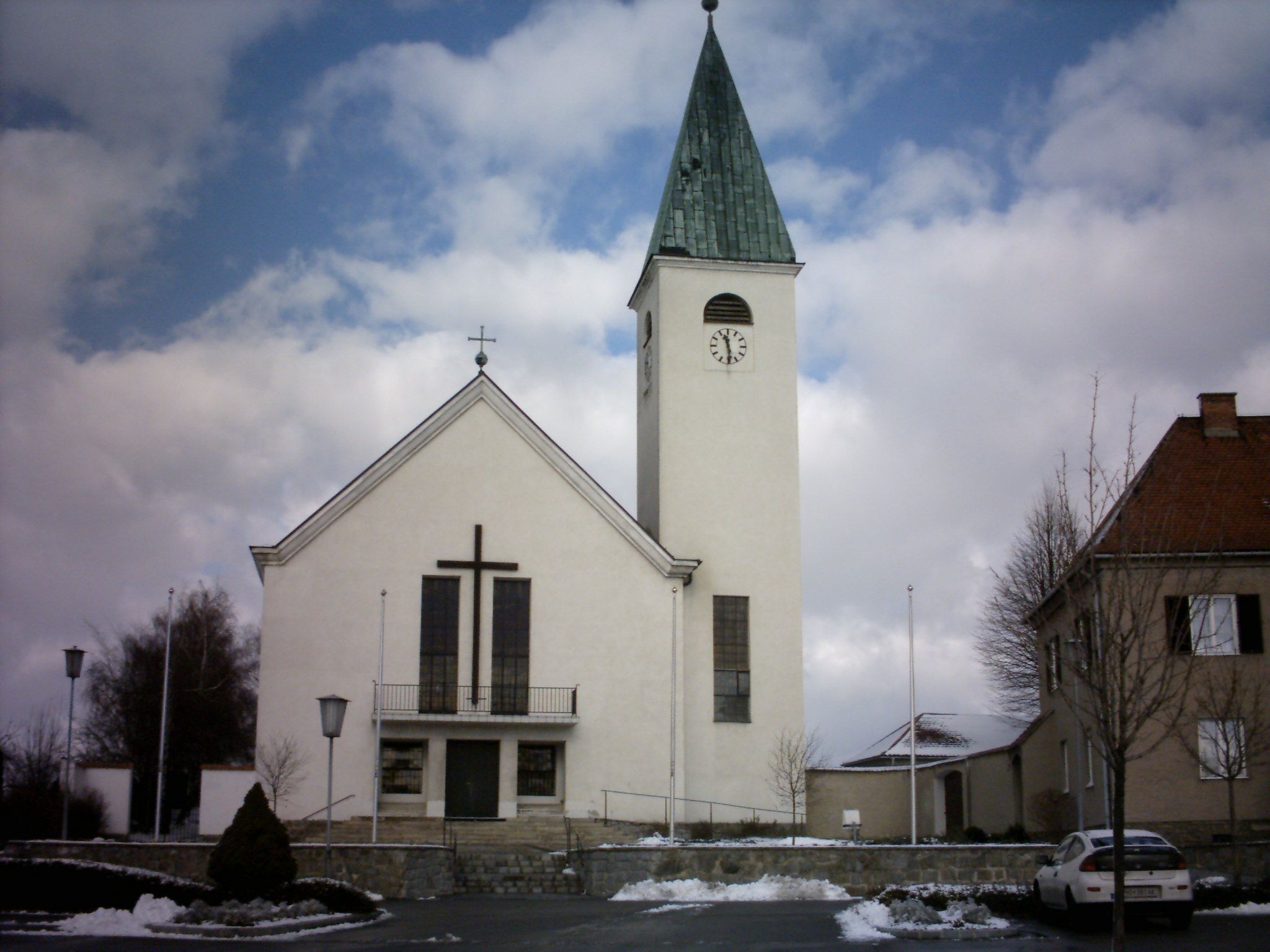 Kirche mit Turm und Uhr in Sigmundsherberg, umgeben von Schnee und Wolken.