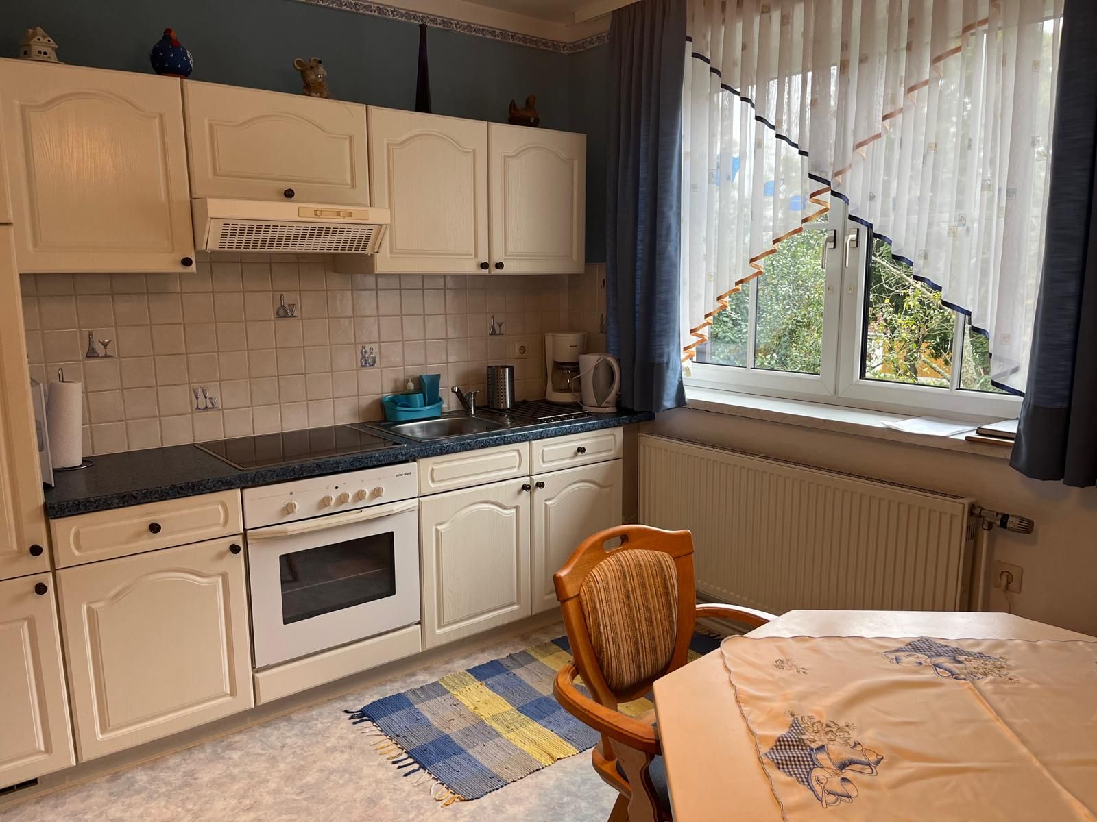 Küche mit weißen Schränken, Herd, Spüle und Fenster mit Vorhängen.