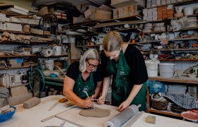 Zwei Frauen arbeiten an einem Tonstück in einer Keramikwerkstatt.