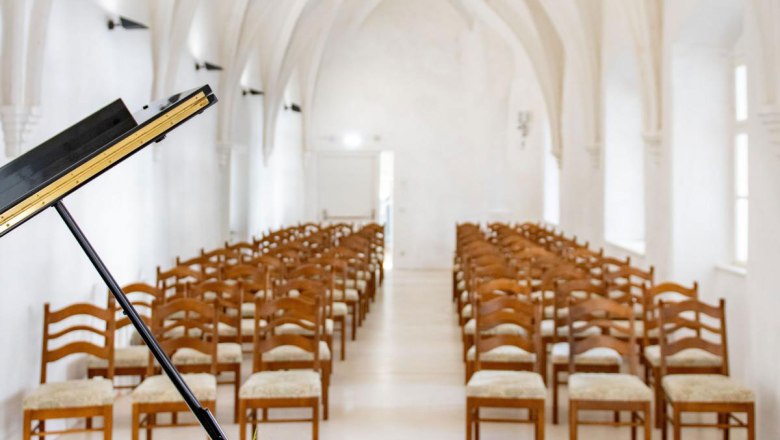 Ein Fl&uuml;gel mit Blumenarrangement steht in einer gotischen Halle mit gew&ouml;lbter Decke und Reihen von Holzst&uuml;hlen.