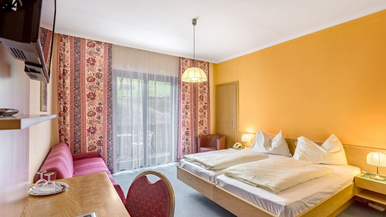 Hotelzimmer mit Doppelbett, gelben Wänden, rotem Sofa und Balkon.