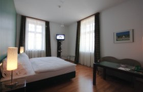 Ein Hotelzimmer mit Doppelbett, zwei Fenstern, einem kleinen Fernseher und einem Tisch mit Stuhl.