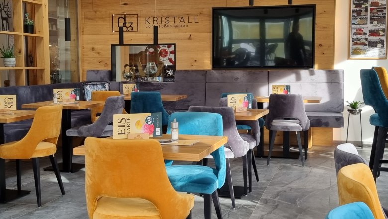 Innenansicht eines modernen Caf&eacute;s mit bunten Samtst&uuml;hlen und Holzw&auml;nden.