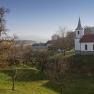 Landschaft mit Kirche und Bäumen bei klarem Himmel.