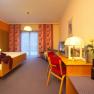 Hotel room with double bed, red chair, TV and lamp on a table. Yellow wall and curtains with a floral pattern.