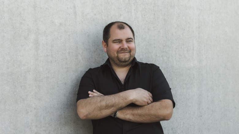 Mann in schwarzem Hemd lehnt an einer Betonwand.