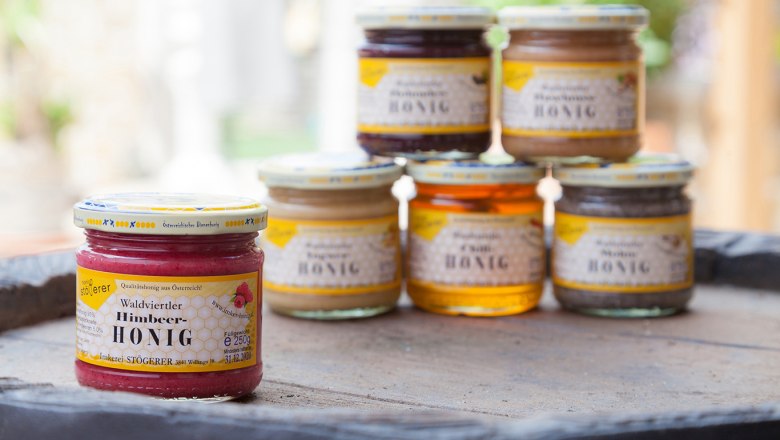 Verschiedene Honiggläser auf einem Tisch, im Vordergrund Himbeer-Honig.