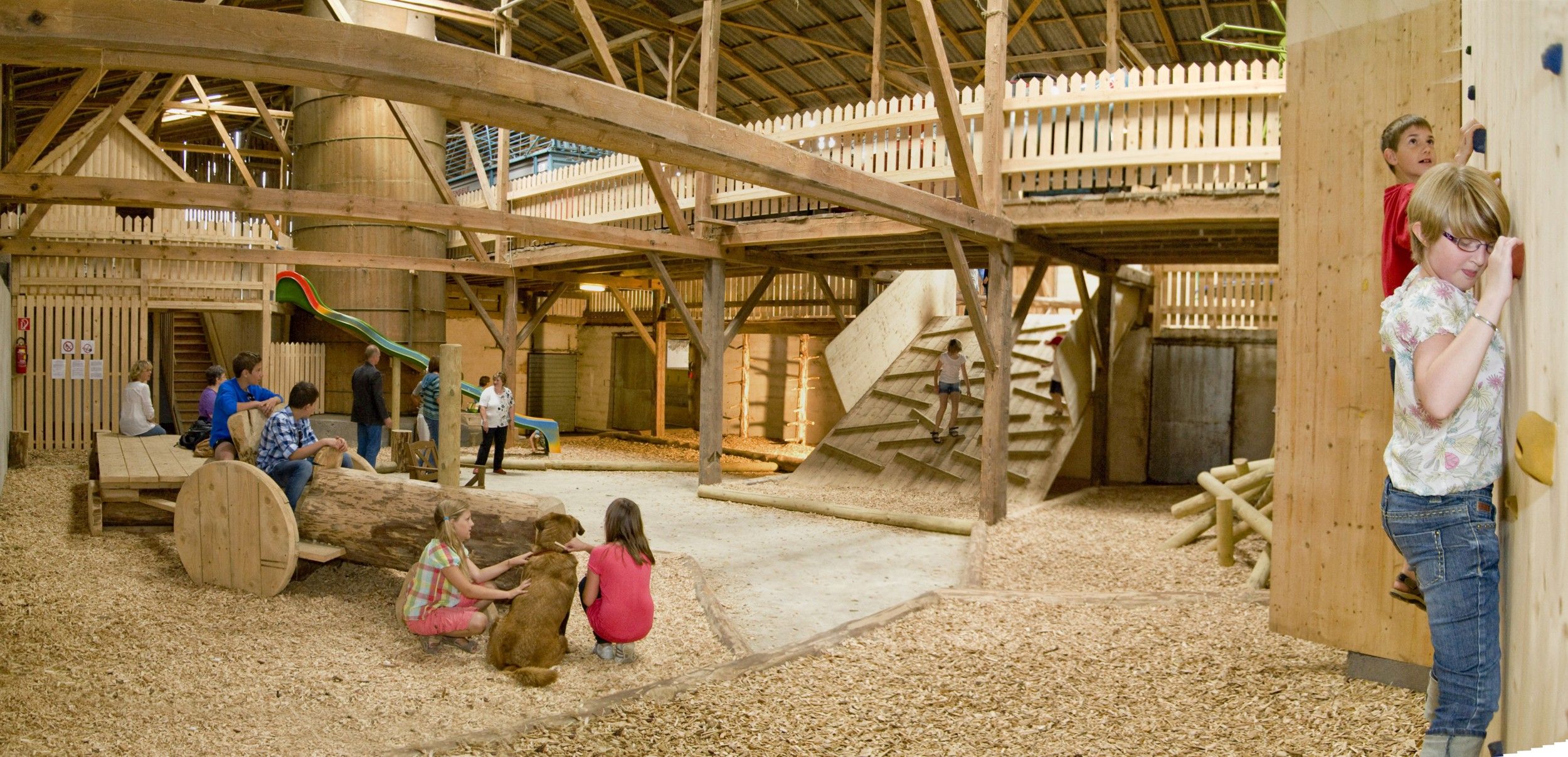 Kinder spielen in einem Indoor-Spielplatz mit Holzkonstruktionen und Rutsche.