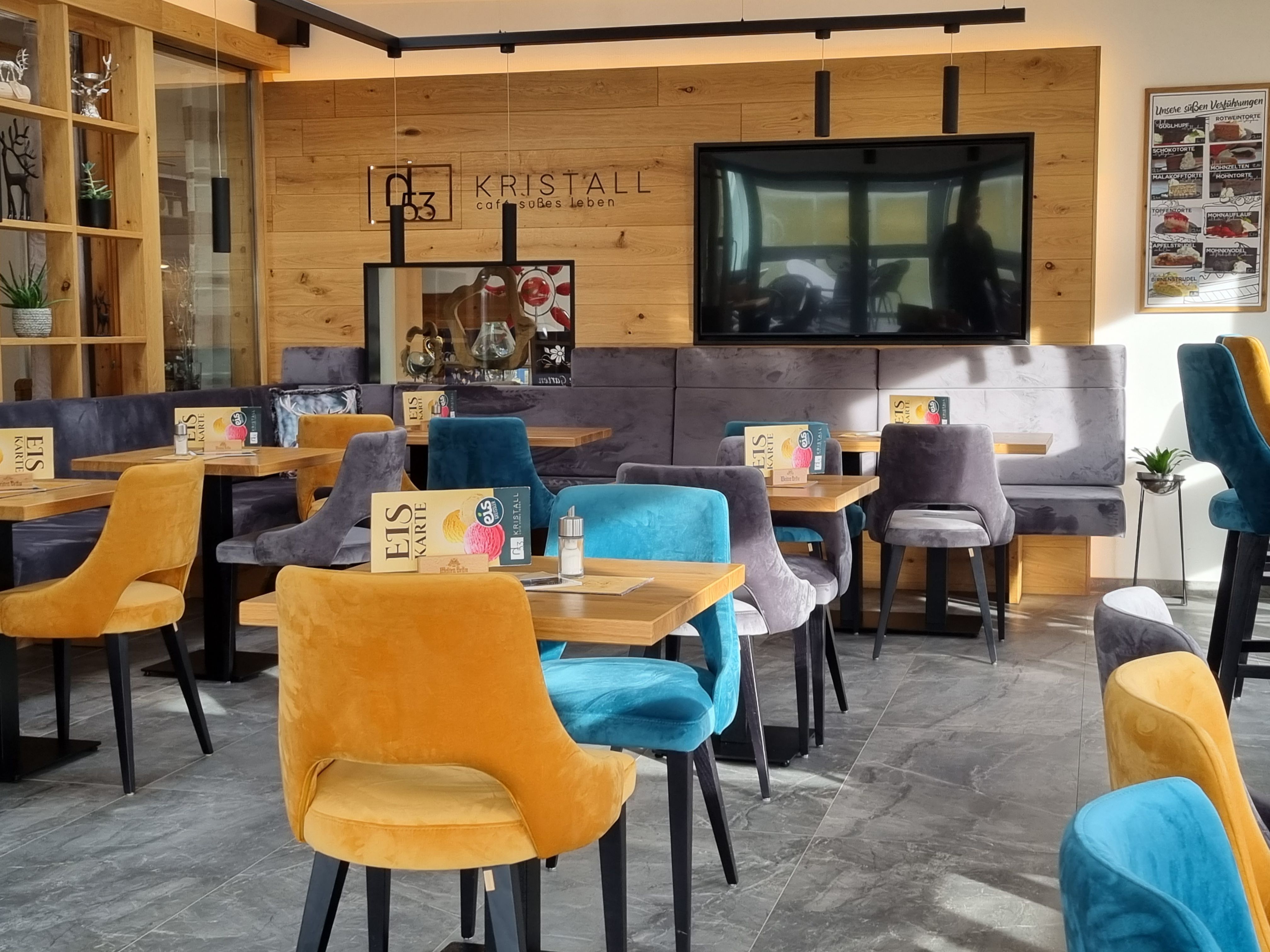 Innenansicht eines modernen Cafés mit bunten Samtstühlen und Holzwänden.