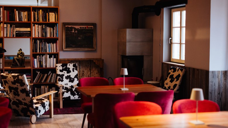 Gemütlicher Raum mit Kamin, Bücherregal, roten Sesseln und Kuhfellstühlen.