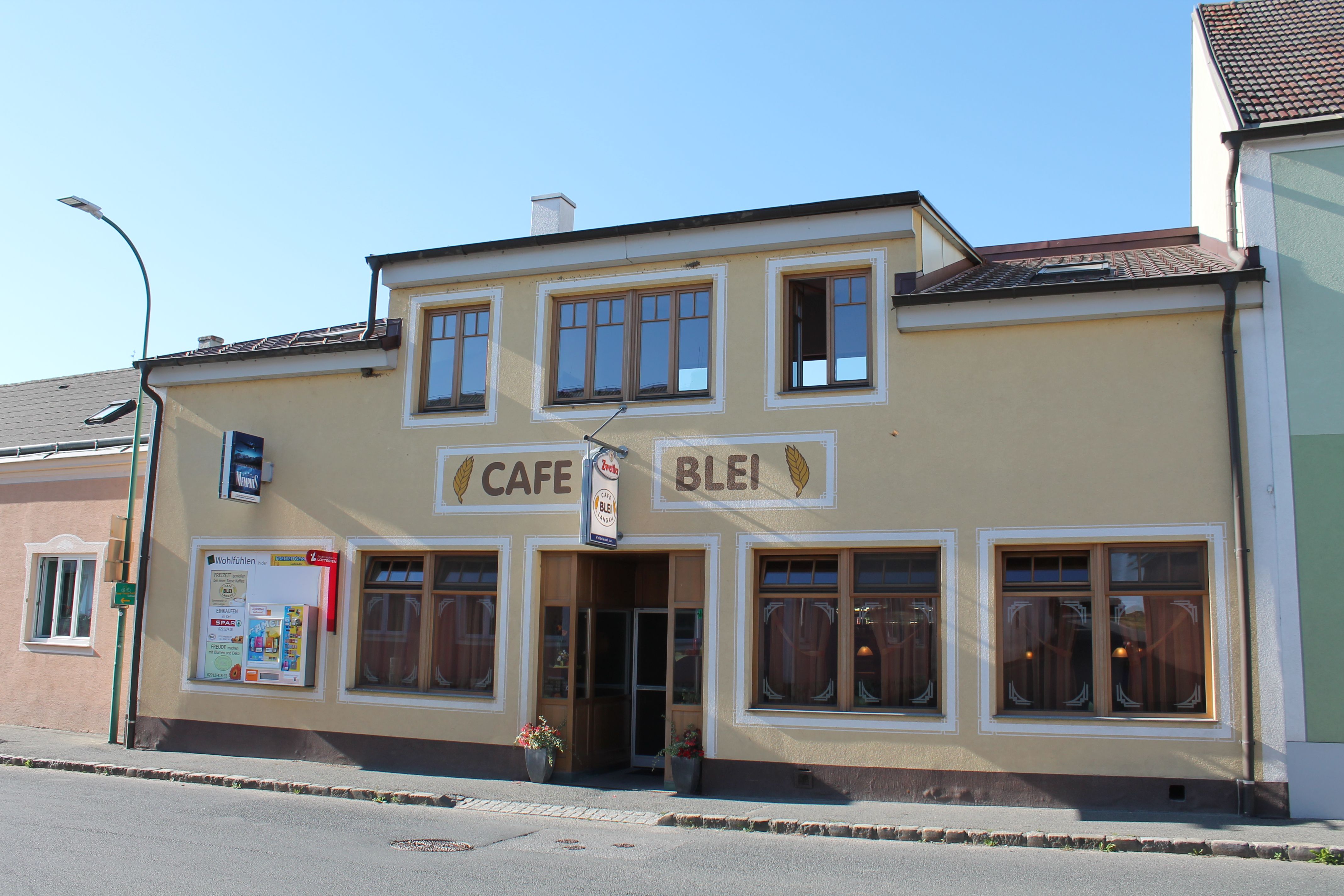 Außenansicht des Café Blei mit gelber Fassade und großen Fenstern.