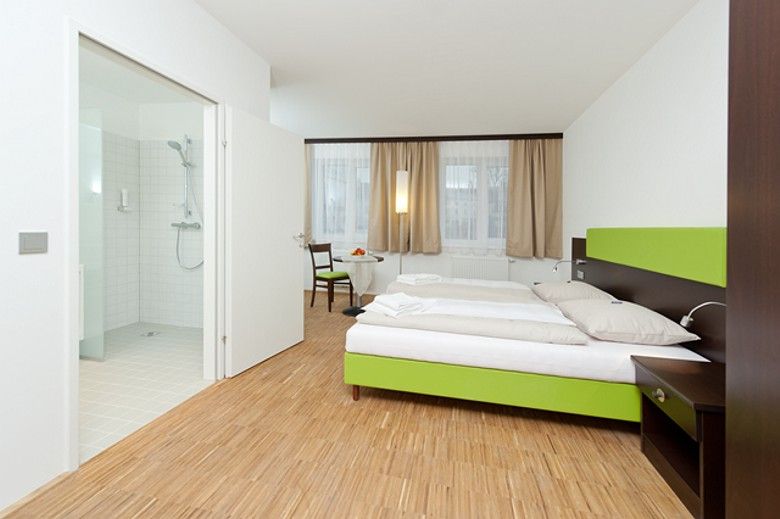 Modernes Hotelzimmer mit Doppelbett, Holzboden und angrenzendem Badezimmer.