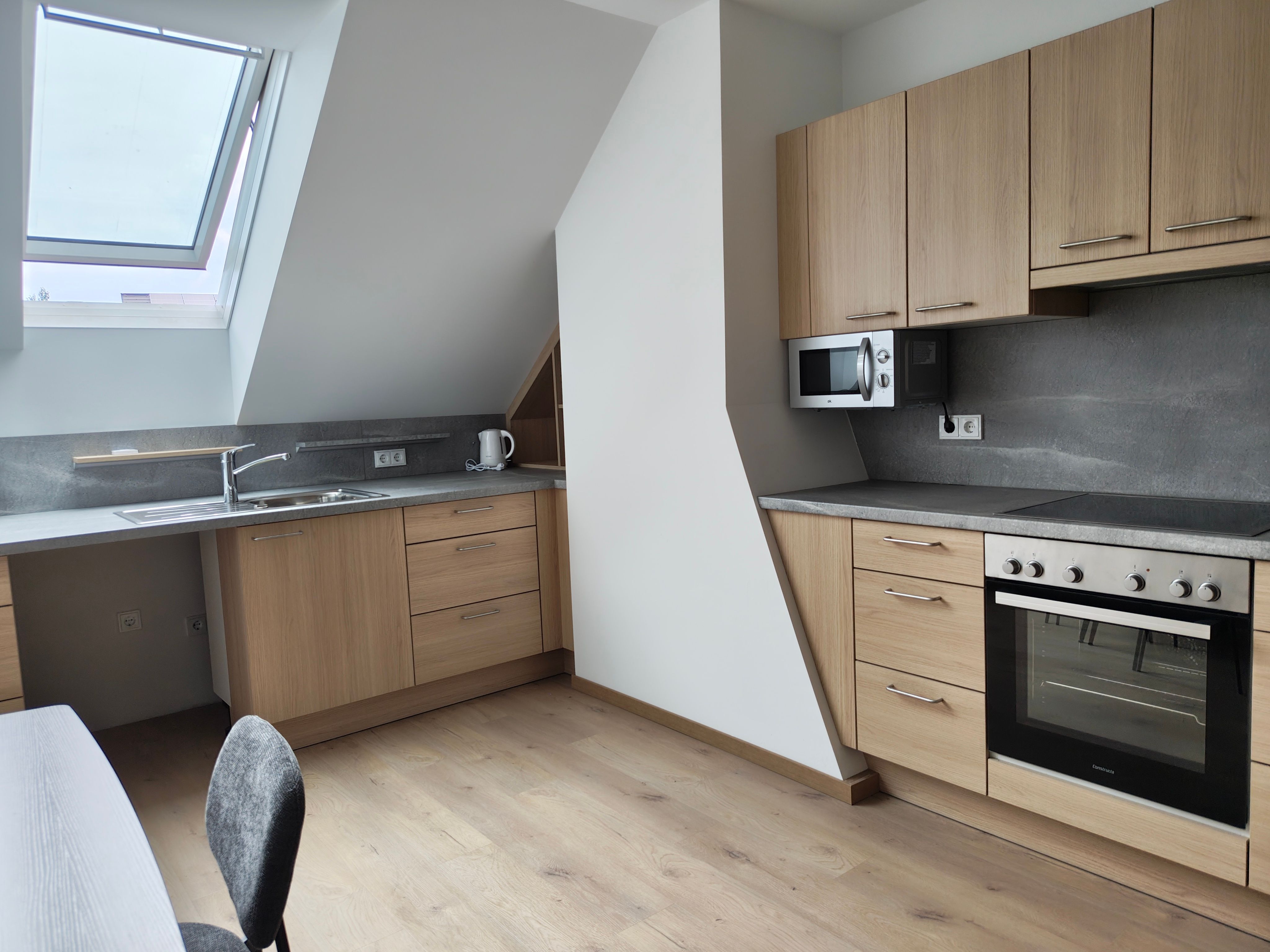 Moderne Küche mit Holzfronten, grauer Arbeitsplatte, Dachfenster, Backofen, Mikrowelle und Spüle.