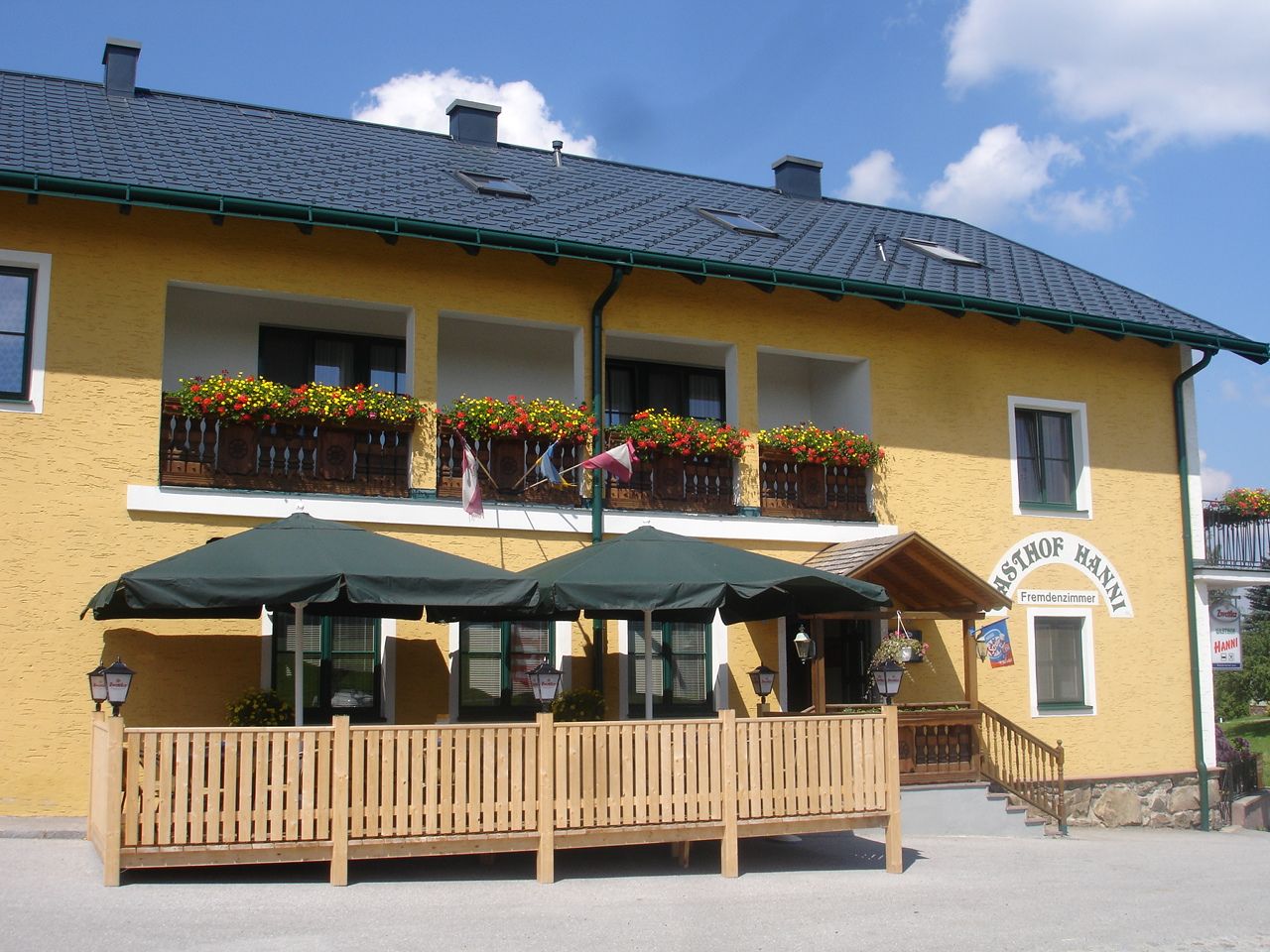 Gelbes Gebäude mit Balkon, Blumen und Terrasse mit Sonnenschirmen.