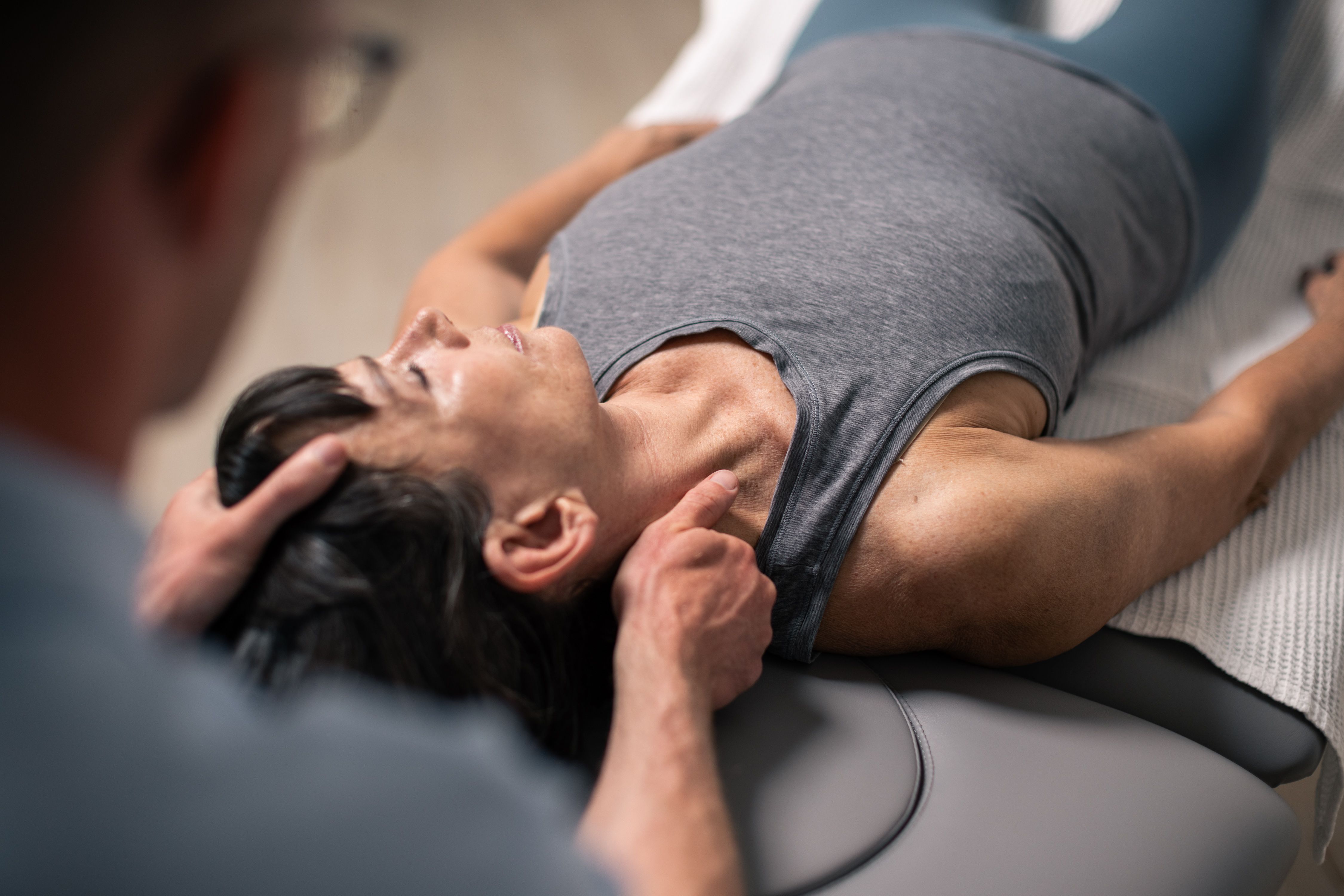 Eine Frau liegt entspannt auf einer Massageliege, während ein Therapeut ihren Nacken massiert.