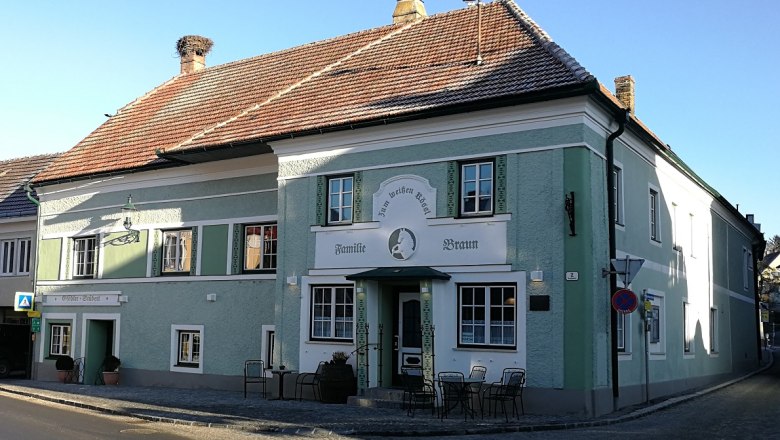 A traditional inn with a green façade and the name 'Zum weißen Rössl'. There are tables and chairs in front of the building.