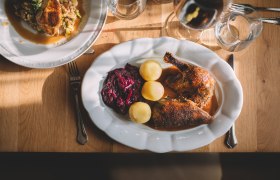 Ein Teller mit gebratener Ente, Rotkohl und Kartoffeln auf einem Holztisch.