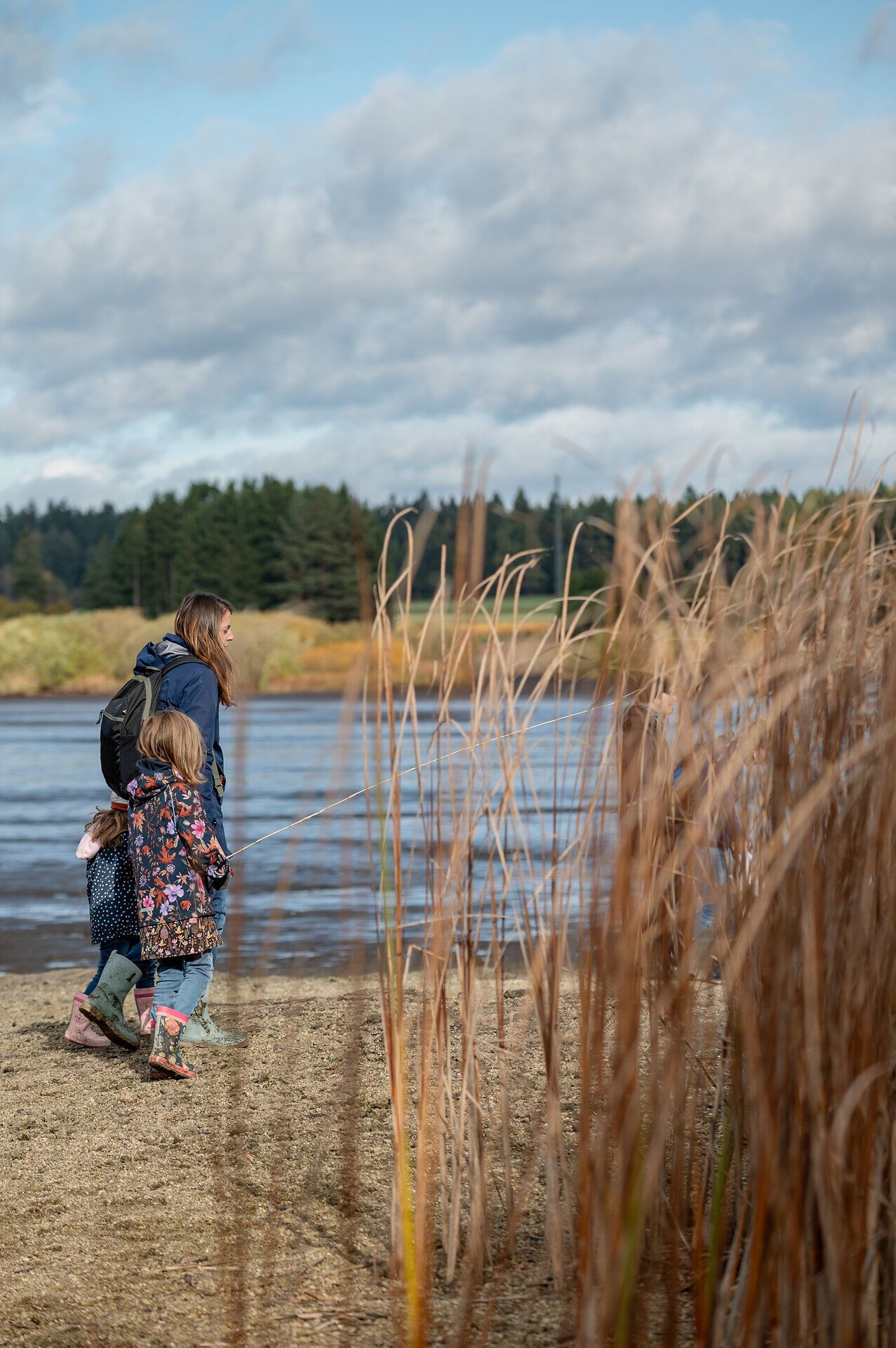 Ein sanfter Wind weht über den Bruneiteich, während eine Mutter mit ihrer Tochter am Ufer entlang spaziert. Die goldenen Schilfrohre wiegen sich im Rhythmus der Natur und schaffen eine friedliche Atmosphäre, die zum Verweilen einlädt.