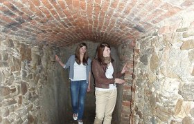 Zwei Frauen in einem schmalen, gemauerten Tunnel mit Ziegeldecke.