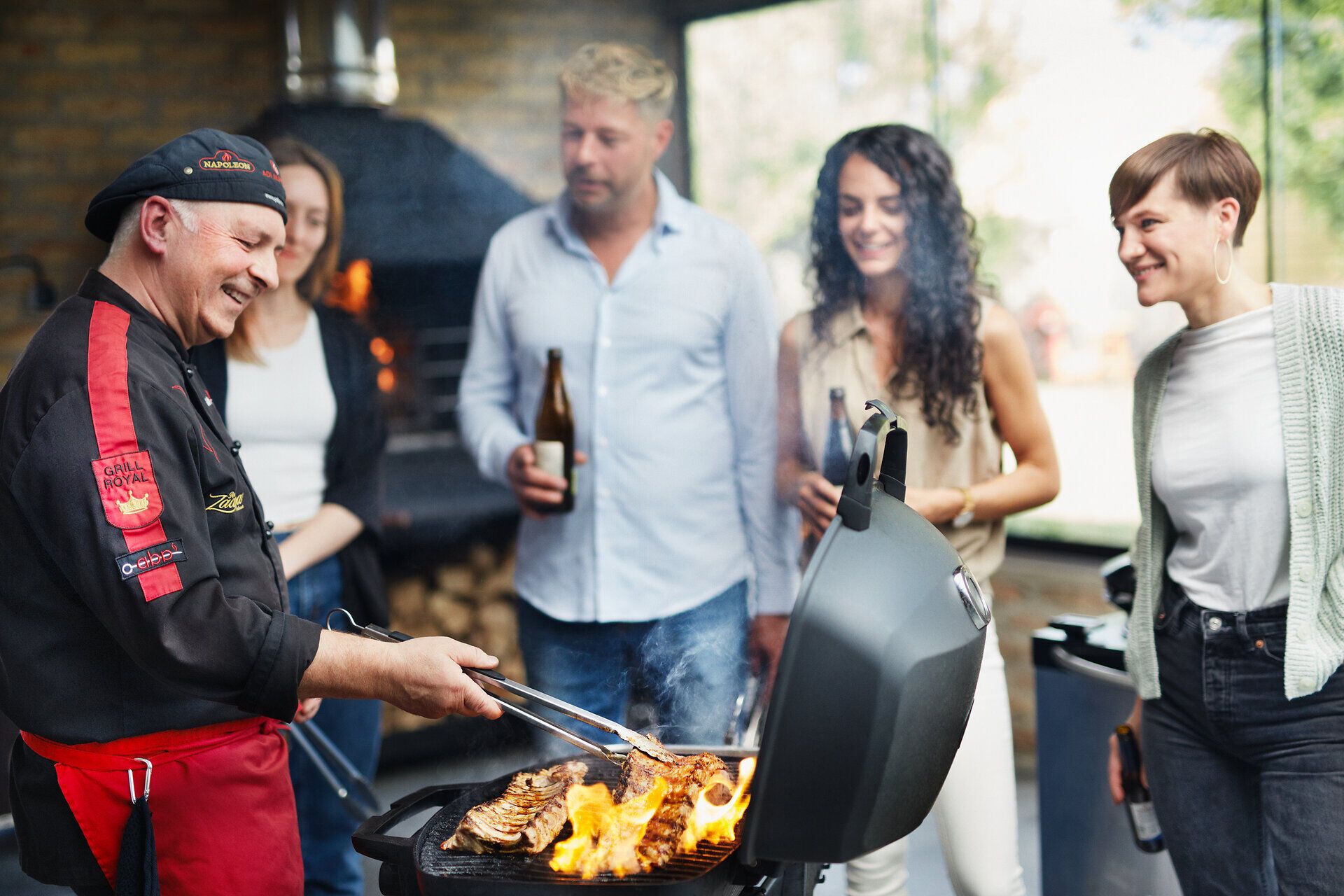 Inmitten einer geselligen Runde wird saftiges Fleisch auf dem Grill zubereitet, während die Flammen lebhaft auflodern. Die Atmosphäre ist geprägt von Lachen und dem verlockenden Duft von frisch gegrillten Köstlichkeiten, die die Vorfreude auf ein gemeinsames Festmahl steigern.