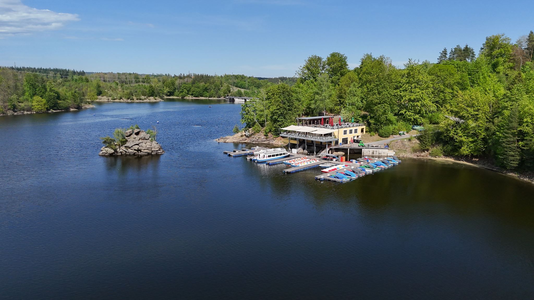 Hotel Ottenstein am See mit Steg, Booten und umgebendem Wald bei sonnigem Wetter.