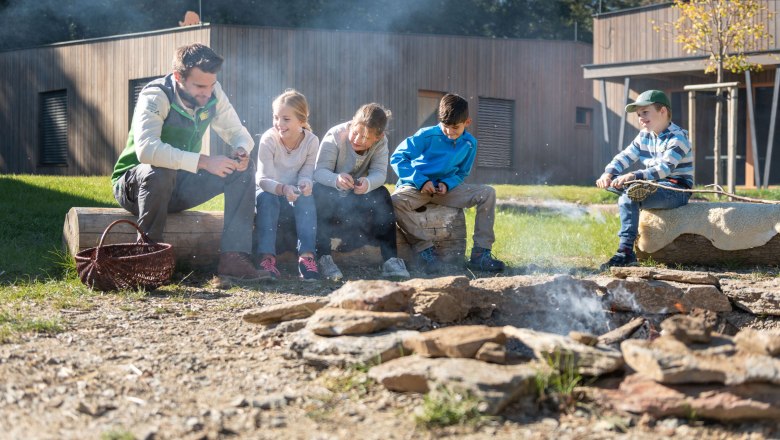 Gruppe von Kindern und einem Erwachsenen am Lagerfeuer im Freien.