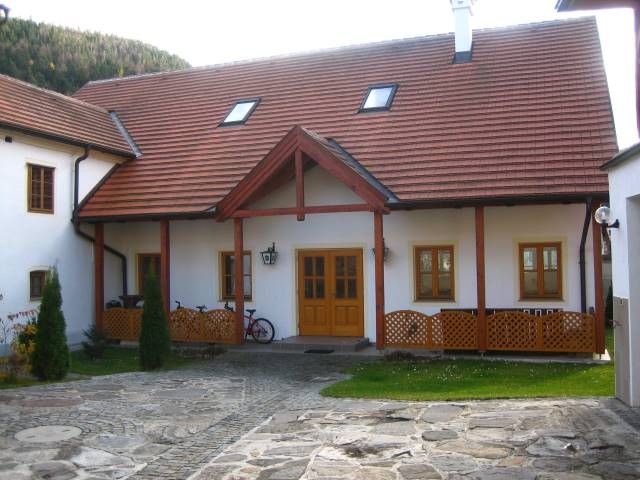 Ein traditionelles Gebäude mit rotem Ziegeldach und Holzelementen, umgeben von einem gepflasterten Hof.