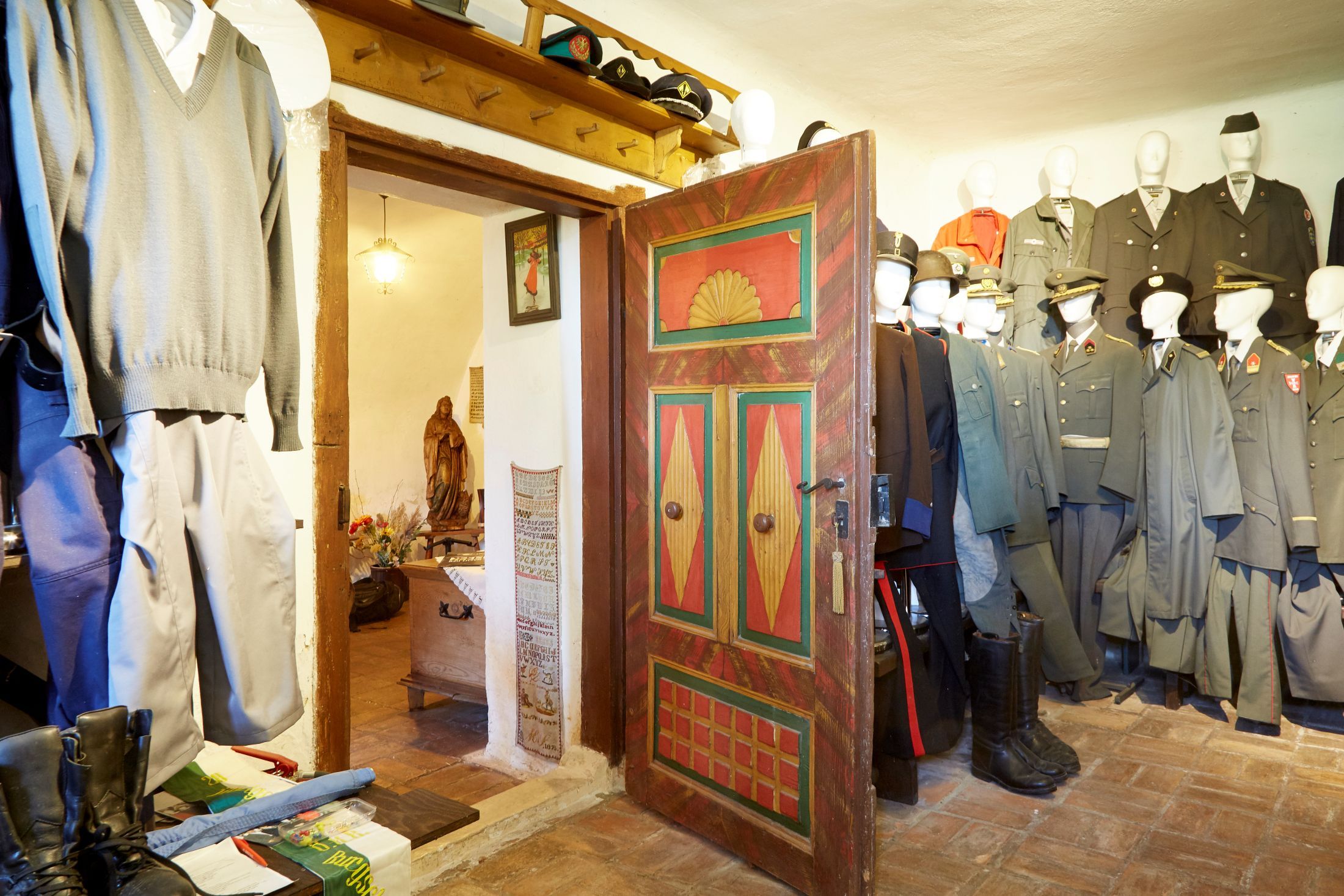 Innenansicht eines Raumes mit alten Uniformen und einer bunt bemalten Holztür.