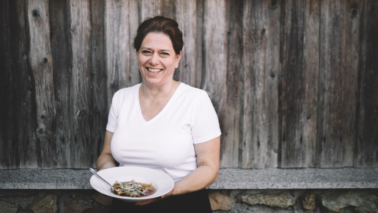 Frau mit weißem T-Shirt hält einen Teller mit Essen vor einer Holzwand.