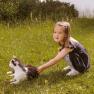 A little girl strokes a black and white cat in a meadow.