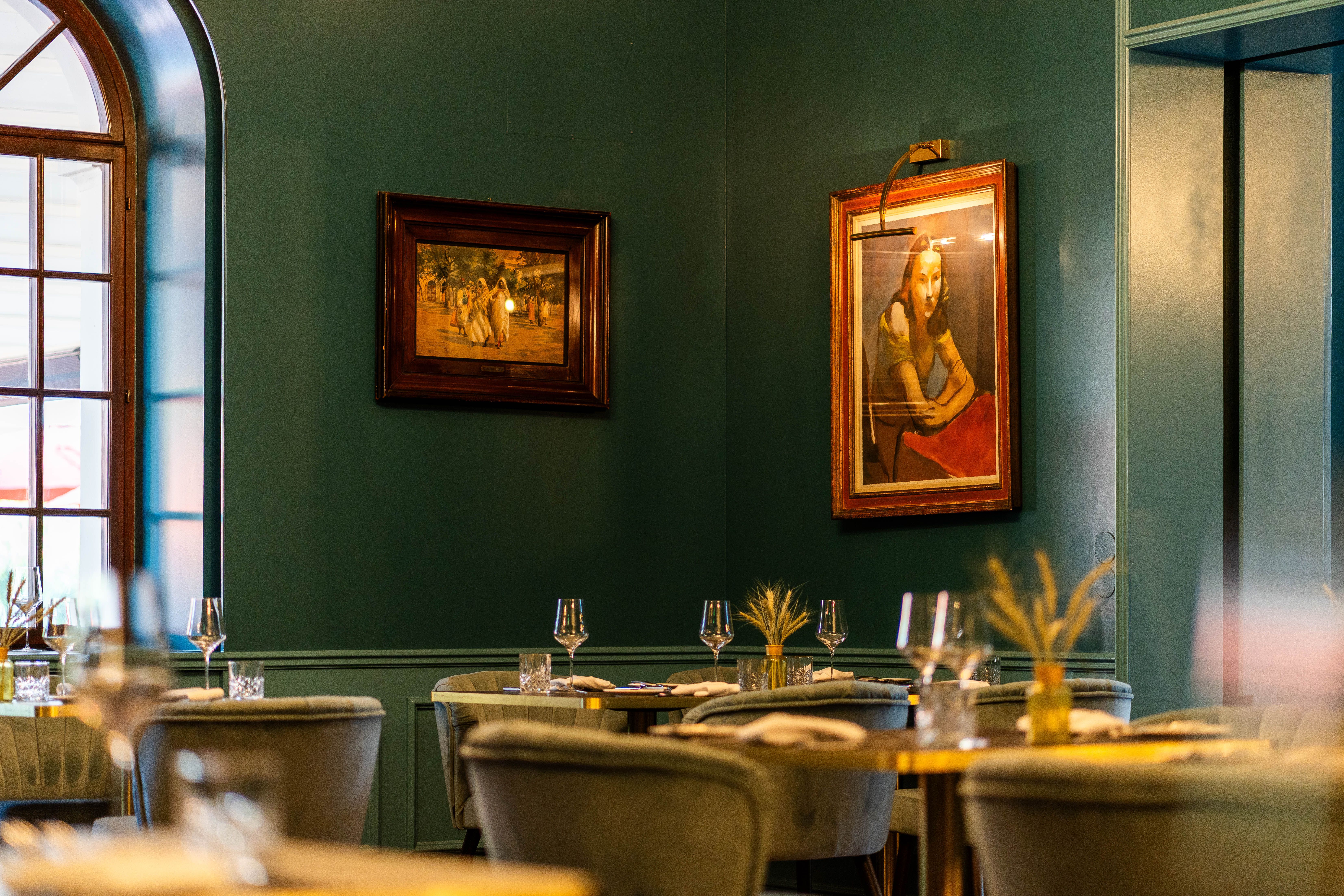 Innenraum des Grafenegg Hotel & Restaurant mit gedeckten Tischen, grünen Wänden, großen Fenstern und gerahmten Bildern.