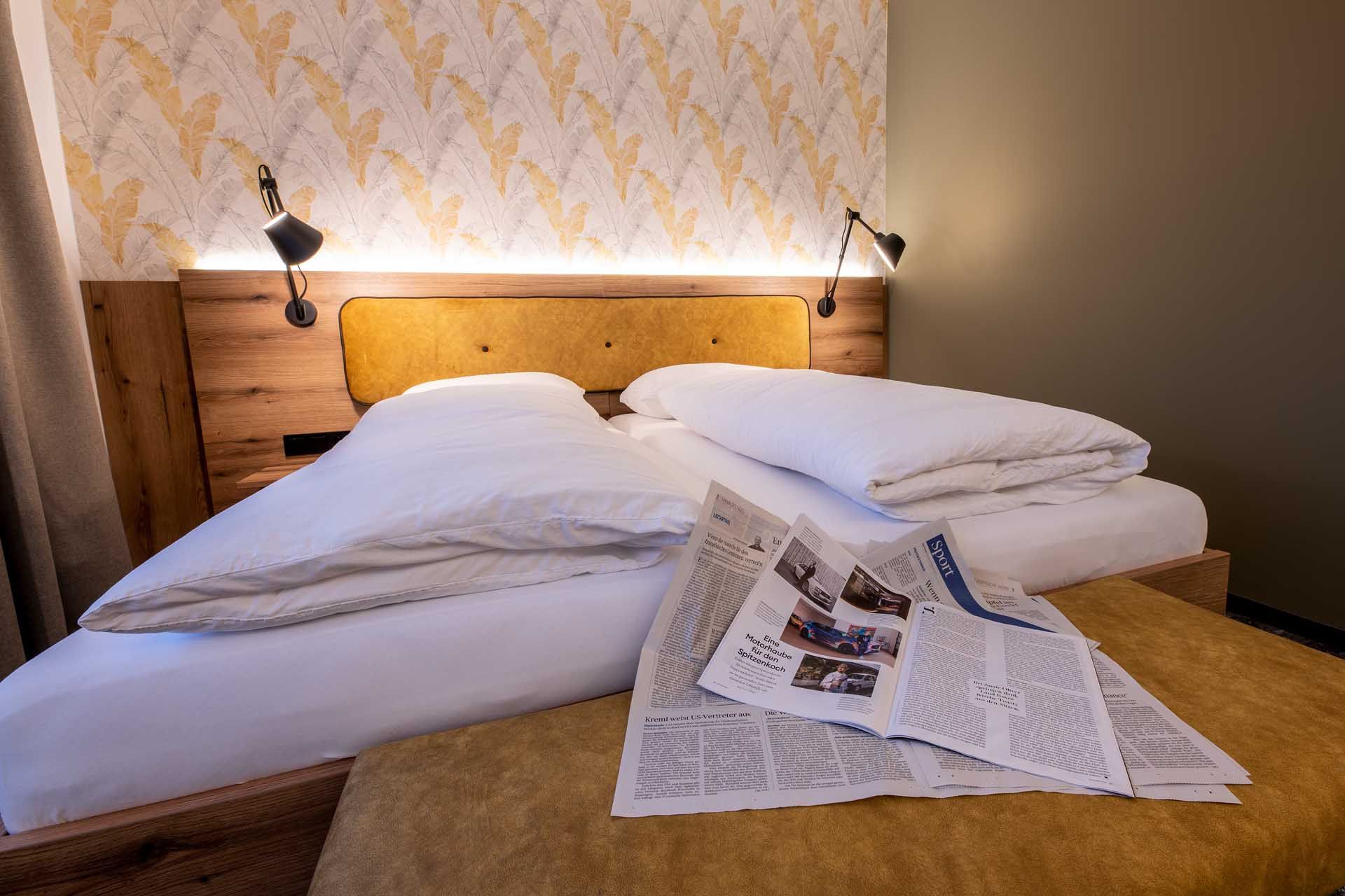 Gemütliches Gästezimmer mit Doppelbett, Zeitungen auf der Bettdecke und stilvoller Tapete im Hintergrund.