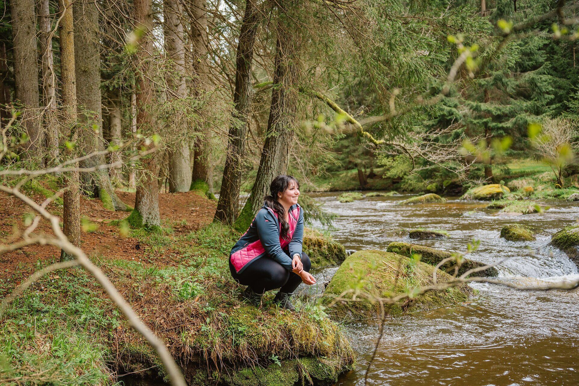 Inmitten der üppigen Natur des Kamptals, wo das sanfte Plätschern des Wassers die Stille durchbricht, genießt eine Wanderin die friedliche Atmosphäre. Umgeben von hohen Bäumen und moosbedeckten Steinen, lädt dieser Ort dazu ein, die Schönheit der Landschaft zu erkunden und die Seele baumeln zu lassen.