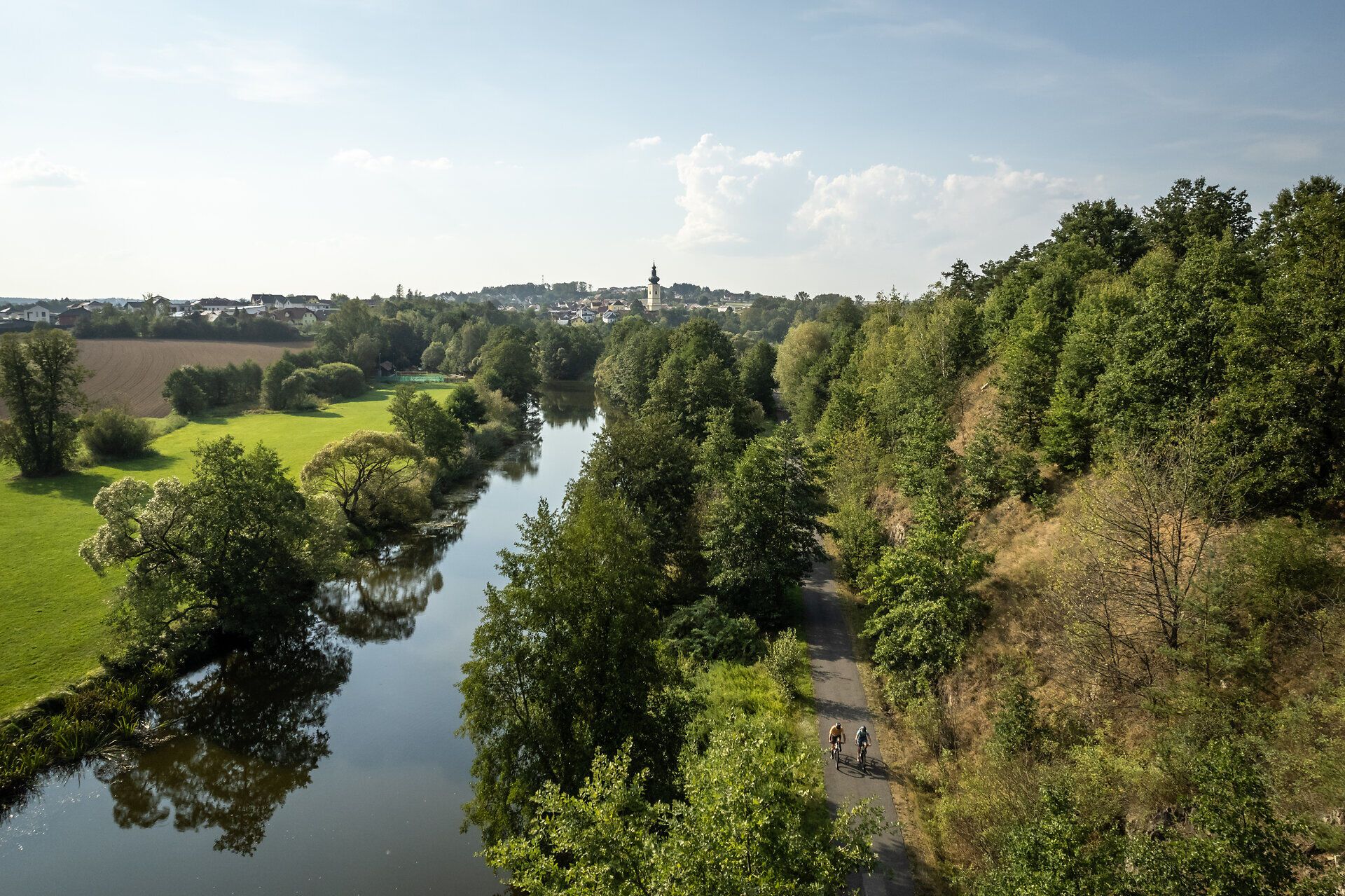 Sanfte Hügel und üppige Wälder umrahmen den glitzernden Fluss, der sich durch die Landschaft schlängelt. Radfahrer genießen die frische Luft und die malerischen Ausblicke, während sie die Ruhe der Natur erleben. Ein perfekter Ort, um dem Alltag zu entfliehen und die Schönheit der Umgebung zu entdecken.