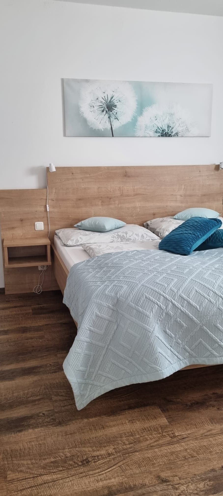 Ein Schlafzimmer mit einem Doppelbett, Holzboden und einem Bild von Pusteblumen an der Wand.