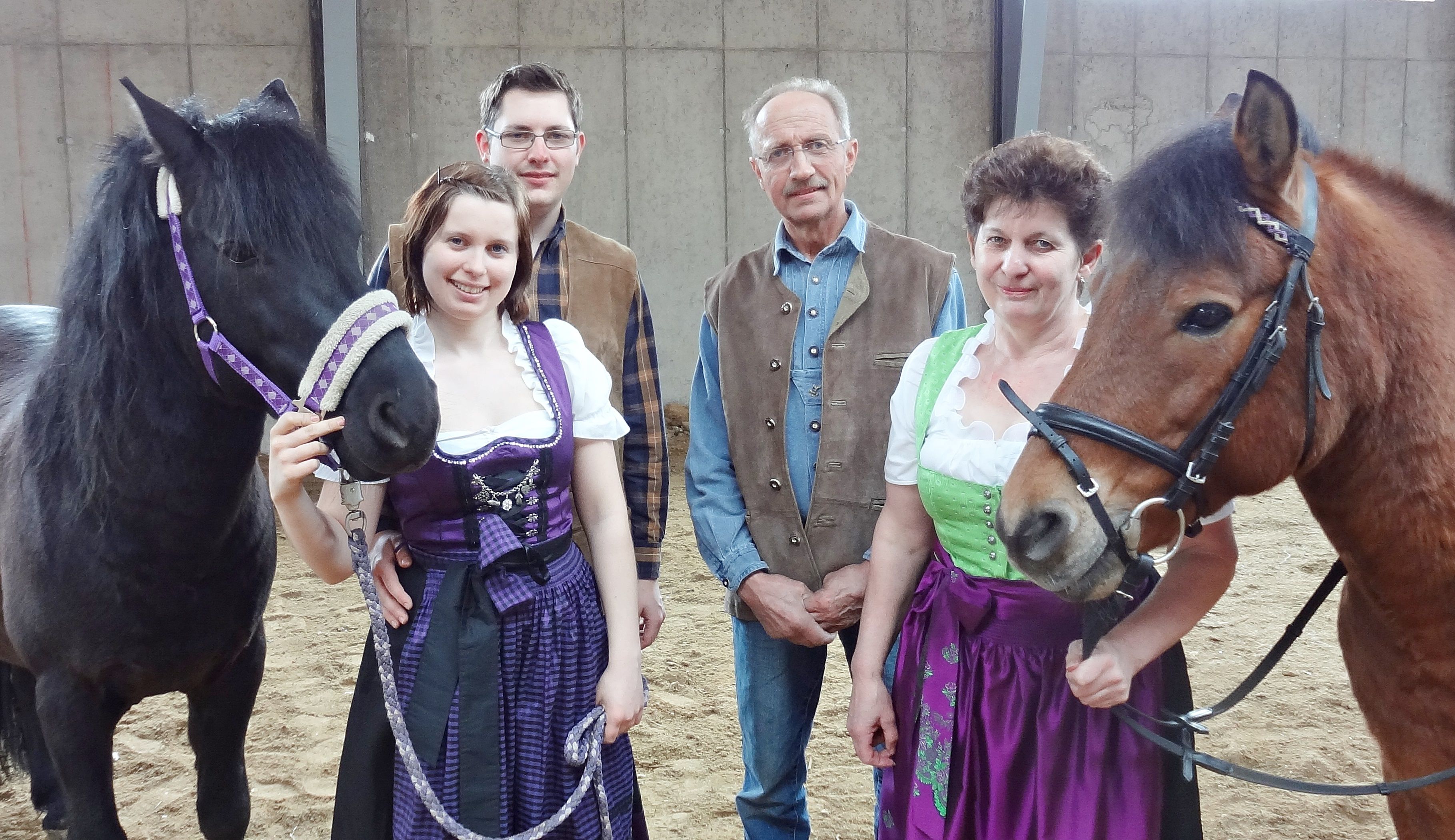 Eine Familie in traditioneller Kleidung steht mit zwei Pferden in einer Reithalle.