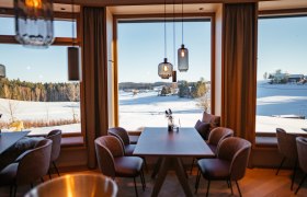 Innenansicht eines modernen Restaurants mit großen Fenstern und Blick auf eine verschneite Landschaft.