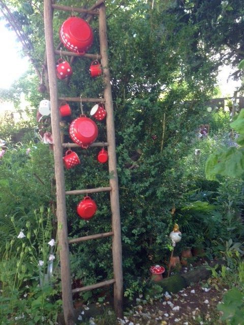 Eine Holzleiter im Garten, behängt mit roten Töpfen und Tassen mit weißen Punkten.