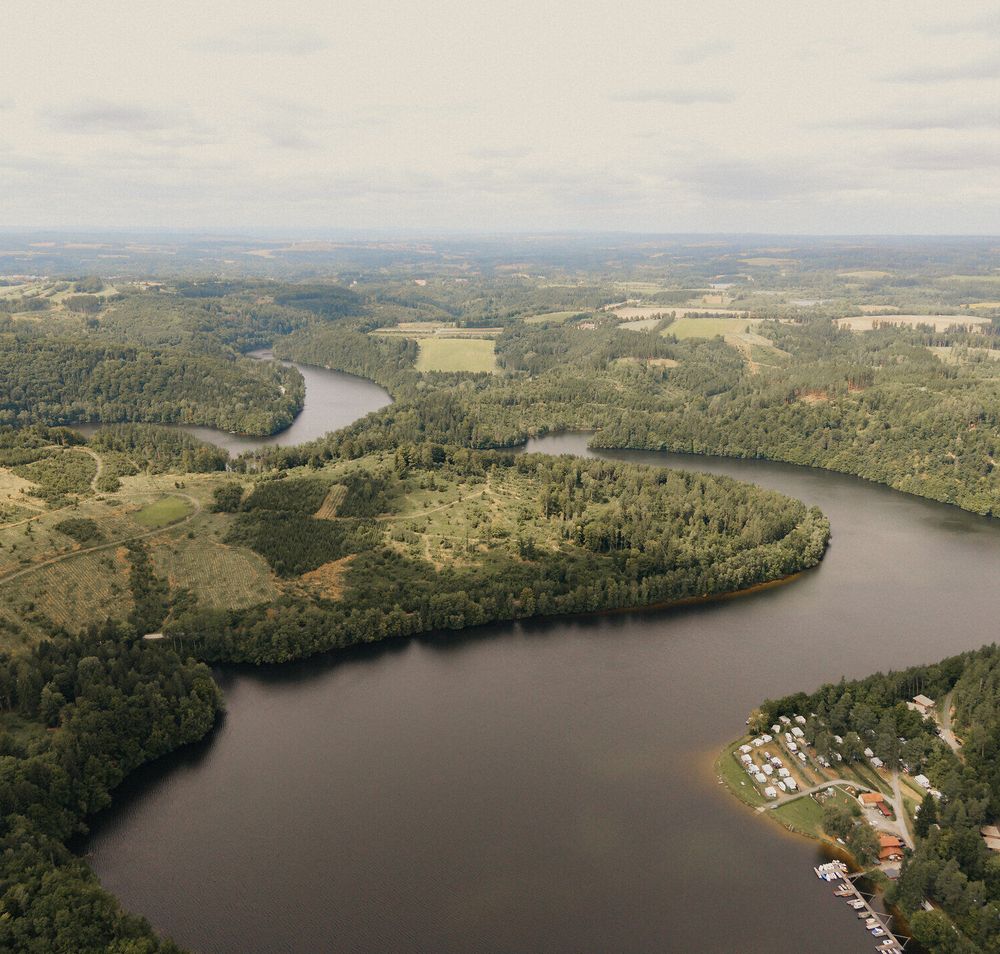 Drohnenaufnahme des Stausees Dobra im Waldviertel; der See schlängelt sich durch bewaldete Landschaft mit Buchten, Wiesen und einem kleinen Uferbereich mit Stegen.
