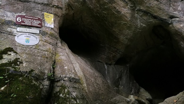 Eingang der Gudenushöhle mit Schildern an der Felswand.